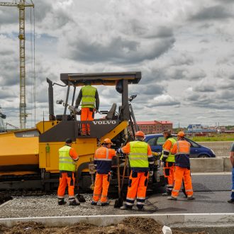 Abbigliamento alta visibilità Tyumen Russia - June 1 2017: JSC Mostostroy-11. Construction of two-level outcome on bypass road on Fedyuninskogo and Permyakova streets intersection. Road rollers compressing sand to highway construction